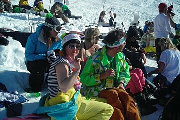 A group of people are sitting in the snow and one of them is wearing a green jacket